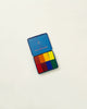 A blue Stockmar Wax Block Crayons Waldorf Tin Case with a colorful rectangle design resembling a pixelated image in Stockmar colors on the lower half, isolated on a white background.