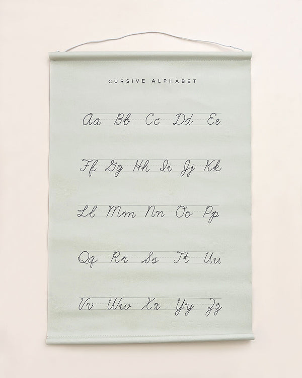 A Gathre Cursive Poster hanging on a wall, featuring uppercase and lowercase letters a to z in black script on a pale green background with the title "cursive alphabet" at the top.