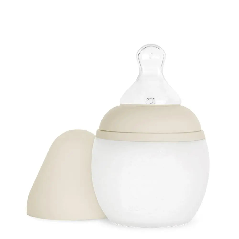 A Medical Grade Silicone Baby Bottle with a removable beige cap, isolated on a white background. The bottle is designed to mimic breastfeeding with its round shape and soft nipple.