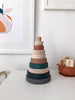 A Wooden Pyramid Stacker - Terracotta with various-sized, pastel-colored rings arranged in order on a white table, adjacent to a small, decorative bowl and underneath a framed abstract art piece.