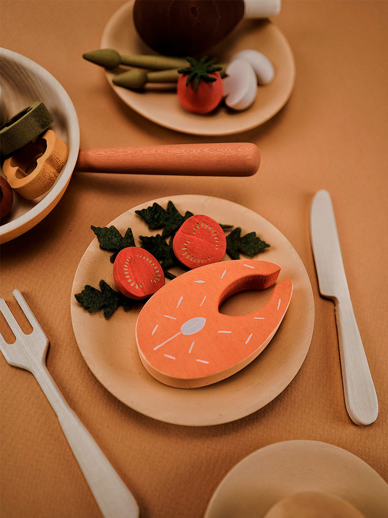 Sabo Concept Handmade Wooden Dinner Set, including a salmon steak and vegetables, is arranged on small plates with cutlery on a beige background.