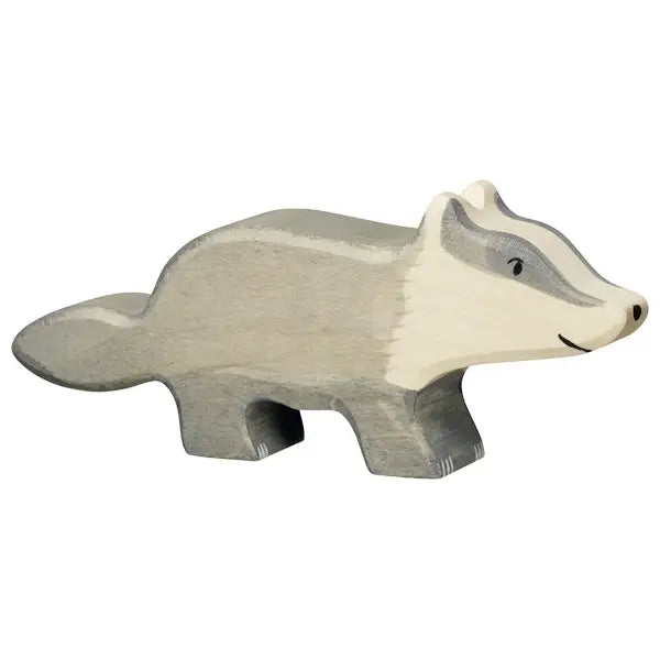 A handcrafted Holztiger Badger, this wooden toy badger is painted in shades of gray with white detailing on its face and tail. Made from maple and beech wood, the badger has a simple, stylized design with a smiling expression and stands on four short legs.