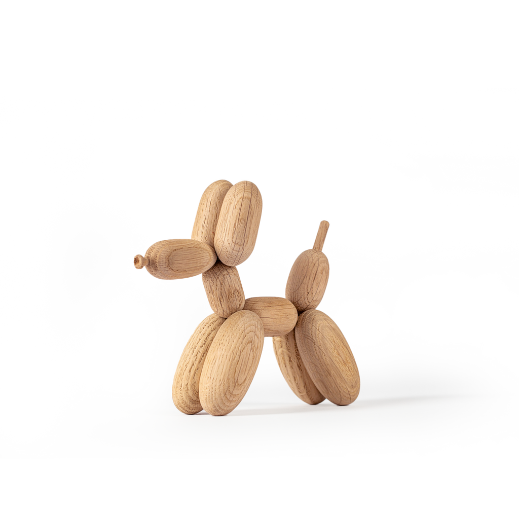 A Boyhood Balloon d'Og, Small Oak toy shaped like a balloon dog, composed of interconnected oval pieces, stands against a white background with grey abstract shapes.
