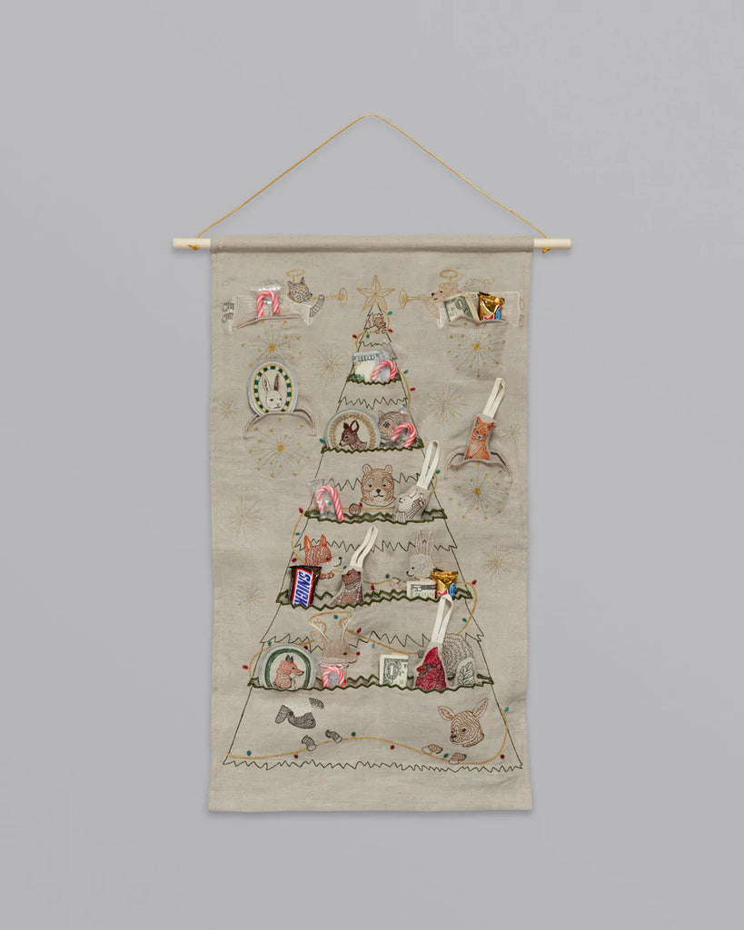A Coral & Tusk Embroidered Advent Calendar shaped like a tree, decorated with pockets featuring various festive designs and small gifts, hanging from a wooden rod against a plain background.