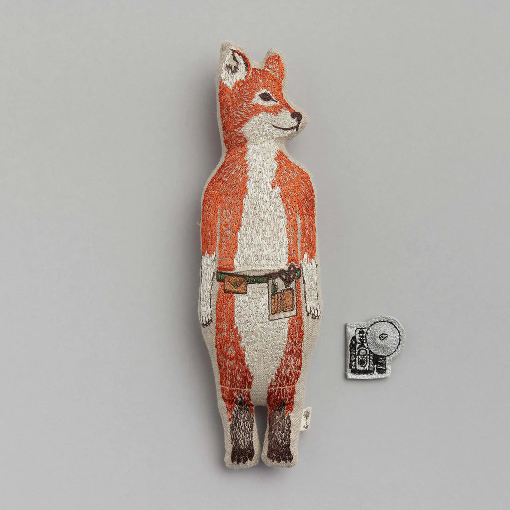 A Coral & Tusk Fox Pocket Doll, painted in orange and white, featuring detailed texture and wearing a belt with a small pouch. Positioned next to a tiny disc, possibly a coin, and strawberries.