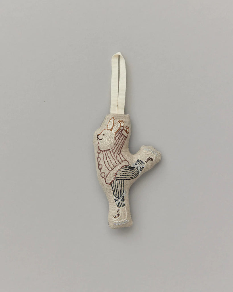 An embroidered Coral & Tusk Ice Skater Bunny Ornament, featuring detailed stitching and patterns on a beige fabric, with a white loop for hanging.