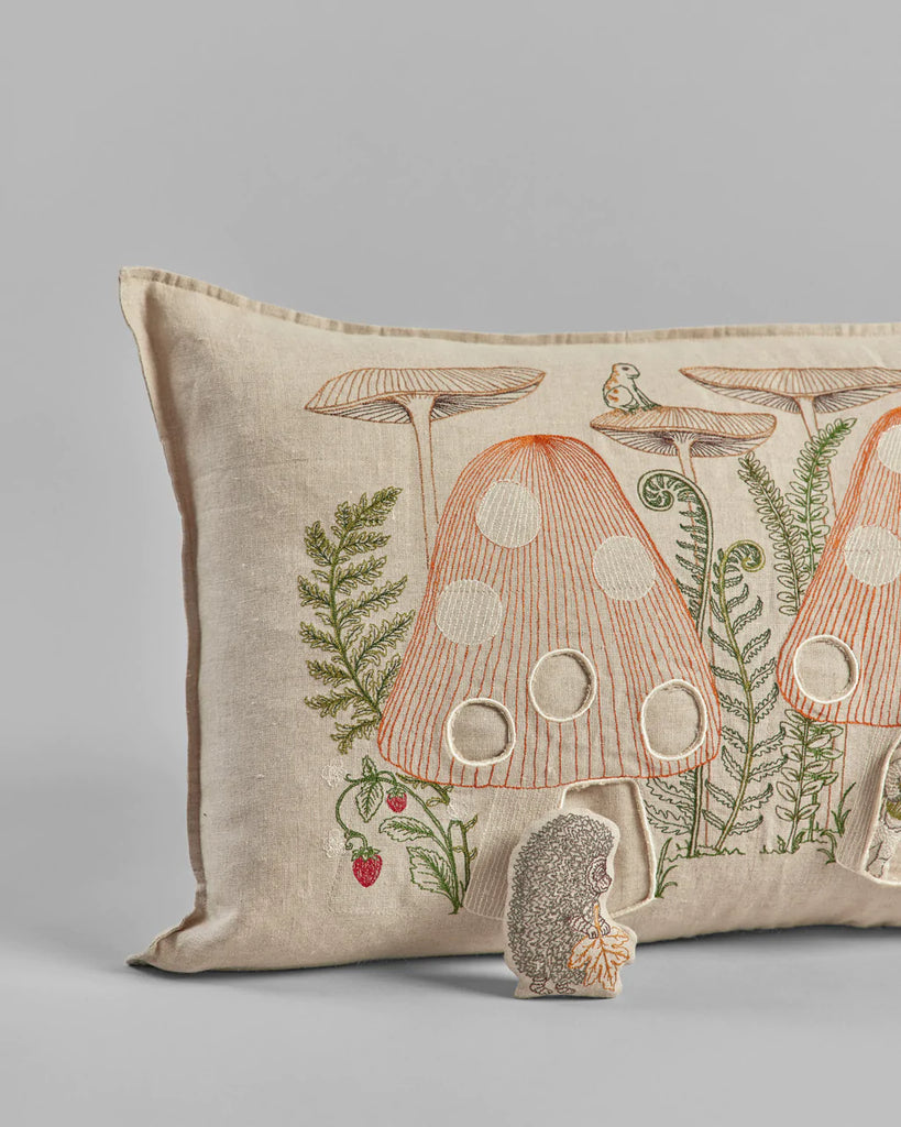 Coral & Tusk Mushroom Mushroom Forest Pocket Pillow with embroidered design of a mushroom house, green ferns, and a foraging chipmunk, set on a neutral beige background.