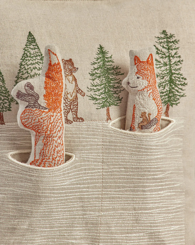 Embroidered forest scene on a Coral & Tusk Winter Foxes pocket pillow, featuring a fox hunt in snow, a raccoon, and pine trees in subtle, earthy colors.