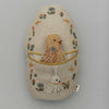 A Coral & Tusk Pocket Easter Egg featuring a chick and a bunny surrounded by colorful flowers and foliage on a neutral background. Both animals are depicted within the contours of the egg-shaped design.