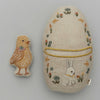 An Coral & Tusk Pocket Easter Egg shaped like an Easter egg, decorated with a rabbit and flowers, alongside a separate small fabric chick. both are set against a plain gray background.