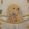 Close-up of a textured fabric featuring an embroidered bird design with a floral pattern on its body, surrounded by golden trim on a Coral & Tusk Pocket Easter Egg background.