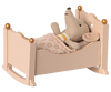A stuffed toy elephant, wrapped in a patterned sleeping bag, lying comfortably in a Maileg Miniature Cradle adorned with golden balls at the bedposts.