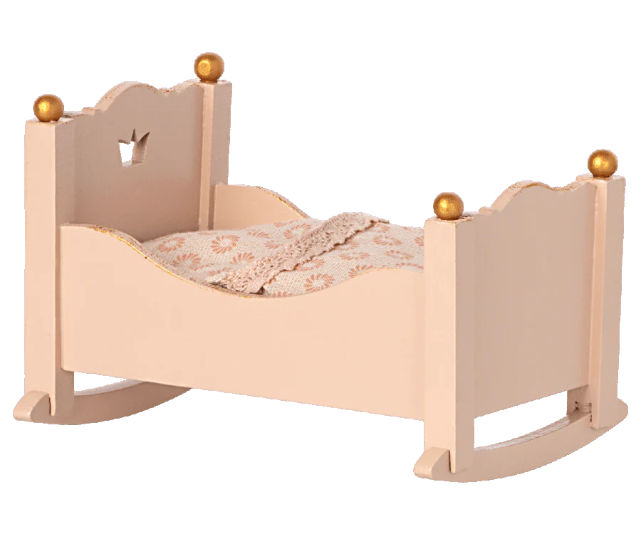 A Maileg Miniature Cradle with a crown design on the headboard, decorated with golden orbs on each post, and featuring an ornate patterned blanket.