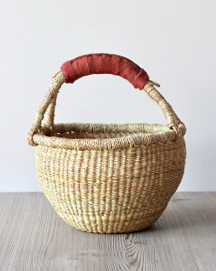 A woven basket with a dark red leather handle.