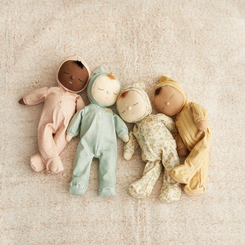 Four Olli Ella Dozy Dinkum Doll - Daydream Editions lying side by side on a soft, beige background, each wearing different patterned outfits.