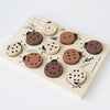 A sustainably sourced wooden tray puzzle featuring fourteen round pieces with various patterns resembling cookies, set on a light background. The board is illustrated with plant motifs and text.