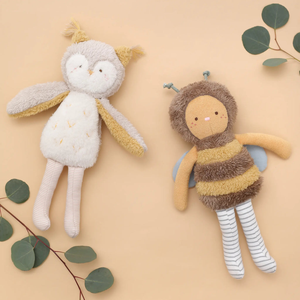 Two Owl Stuffed Animals lie on a beige background surrounded by green leaves in Vietnam, creating a soft and playful scene.