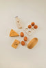 Flat lay of various objects including a Sabo Concept Handmade Wooden Dairy Set, a bottle labeled "milk," a piece of cheese, a carton with six eggs, and non-toxic paint wooden blocks shaped like