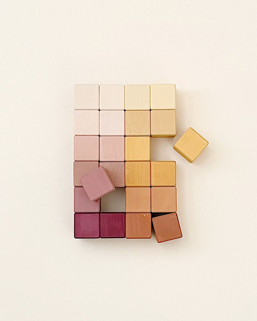 A collection of Marsala Wooden Blocks, painted with non-toxic paint, arranged in a nearly complete square formation on a light background, with one square block detached.