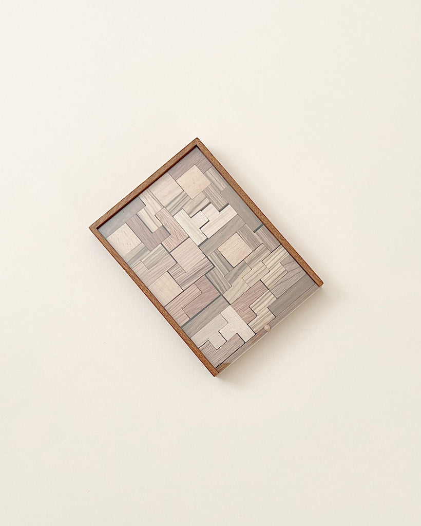 A Wooden Puzzle set, neatly arranged within a square frame on a light background, showcasing various puzzle pieces in shades of gray and brown. Please note this item is a choking hazard.