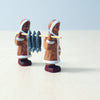 Two Wooden Inuit Sets of elderly women in traditional dresses, carrying a large fish on a pole between them, standing on a light wooden surface against a soft blue background. These handcrafted toys capture charming details.