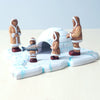 A hand-carved Wooden Inuit Set featuring figures in fur-trimmed parkas around an igloo, displayed on a wooden table with Montessori materials.