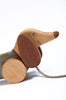 Handmade Pull Along Dog Toy crafted from sustainably harvested birch wood, with wheels, a pull string, and smiling features, set against a plain white background.
