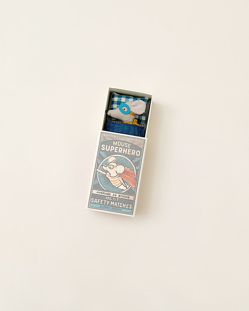 A box of Maileg | Superhero Mouse, Little Brother safety matches on a plain beige background, partially open, revealing blue matches inside and featuring cartoon artwork on the cover.