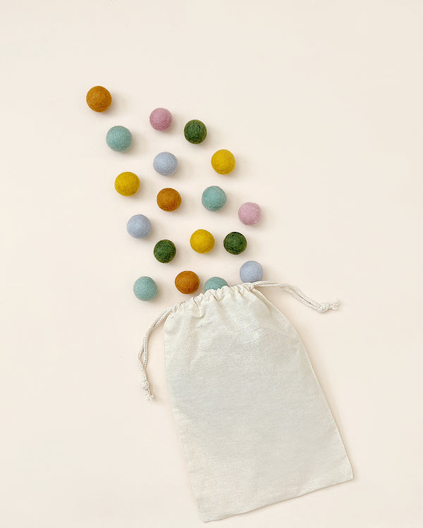 Colored felt balls coming out of a muslin bag on a cream background