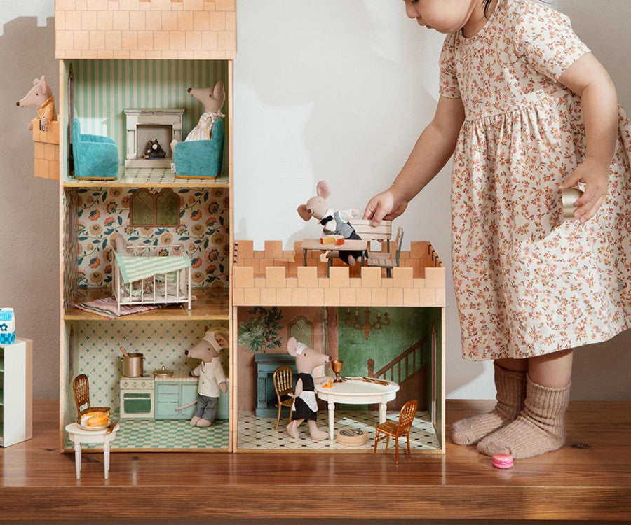 A young child plays with a large, detailed Maileg Castle Hall filled with FSC Paper Mice and miniature furniture, carefully placing a figure on the roof.
