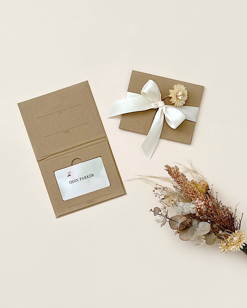 Two elegant gift boxes with satin ribbons and a small bouquet of dried flowers, one box labeled "Gift Card," on a light beige background.
