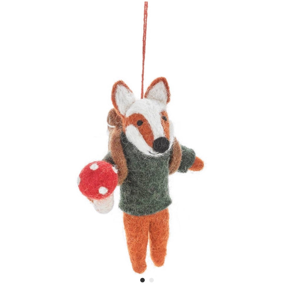 A Handmade Felt Fox Christmas Tree Ornament wearing a green sweater and holding a red and white mushroom, suspended by a red string.