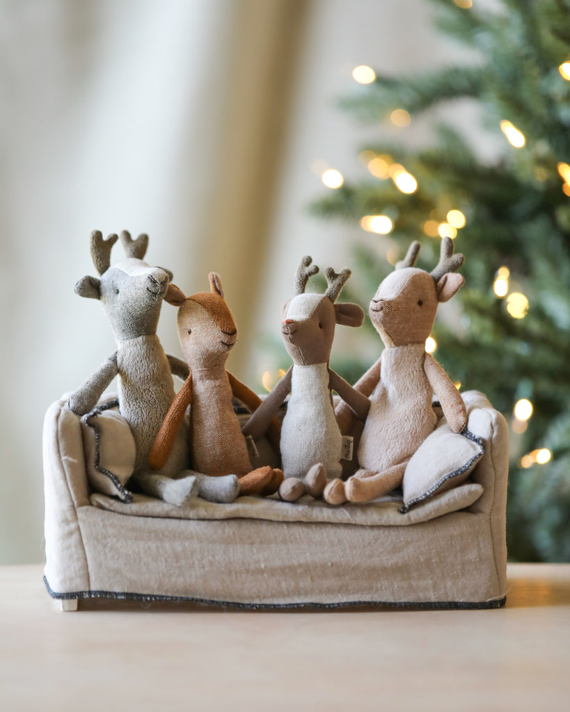 Four small deer stuffed animals sitting on a couch together. 