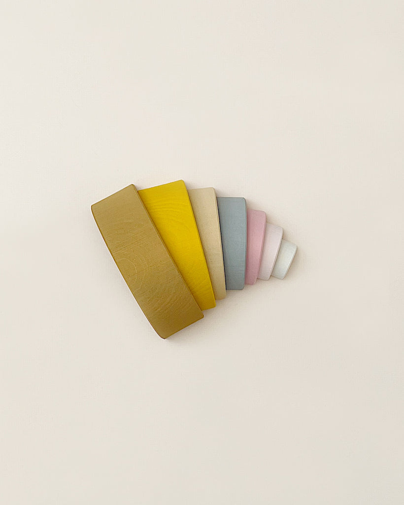 A stacking toy with 7 pastel tone wooden arcs stacked into a rainbow shape. Photographed from an aerial view.