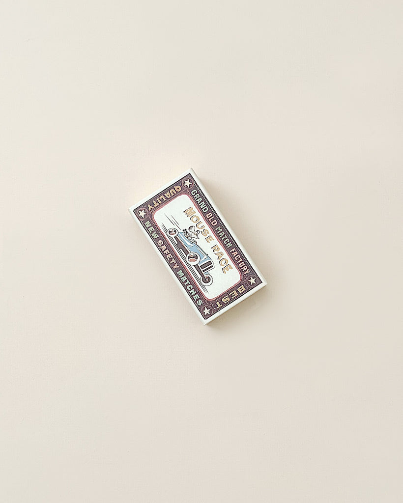 A deck of Maileg | Mouse in a box - Big Brother playing cards lies on a light beige polyester surface, viewed from above. The card box is white with red and blue vintage design elements.