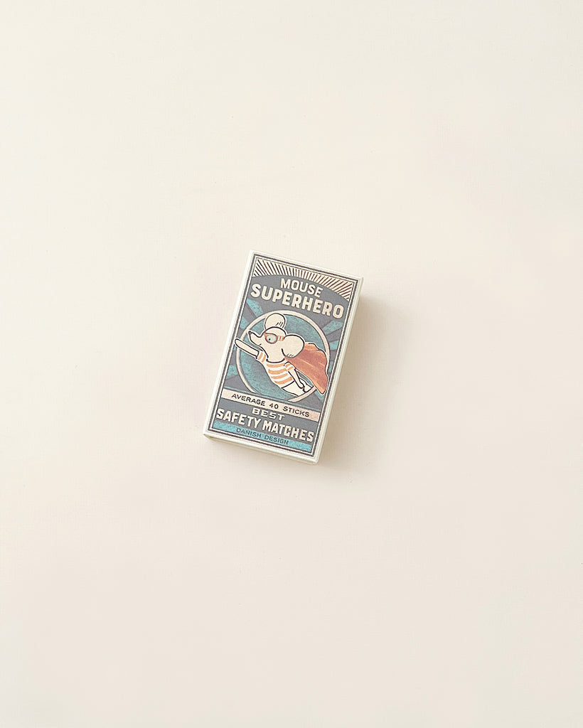 A vintage matchbox labeled "superhero safety matches" with a graphic of Maileg | Superhero Mouse, Little Brother, set against a plain light background.