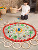 A young child plays with a colorful educational game on the floor, arranging various shaped and colored Grapat Mandala Green Cones within a pattern of red concentric circles.