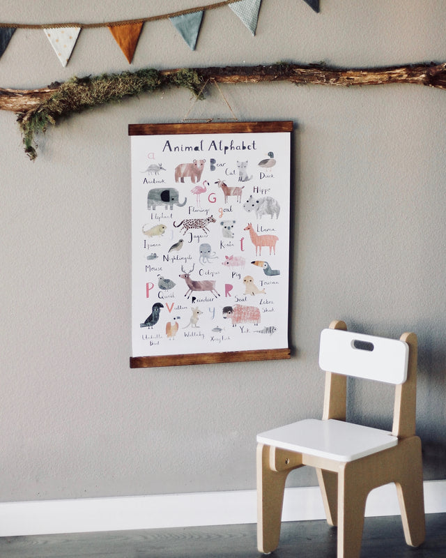 A children's Animal Alphabet Poster framed on a wall above a small wooden chair. The poster includes colorful illustrations of animals corresponding to each letter of the alphabet.