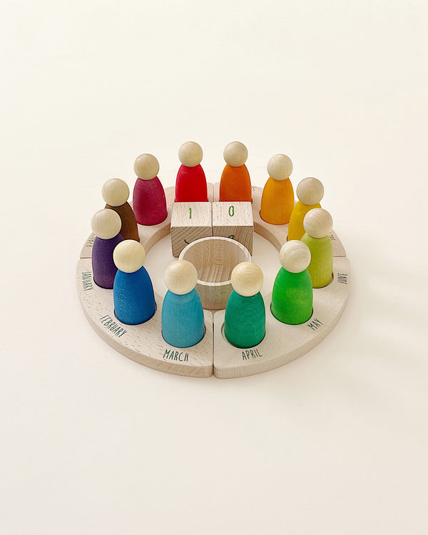 A Grapat Perpetual Calendar with Peg Figures, with colorful pegs representing different months, arranged in a circle around two interchangeable date blocks set at "10." The base is labeled with the months' names.