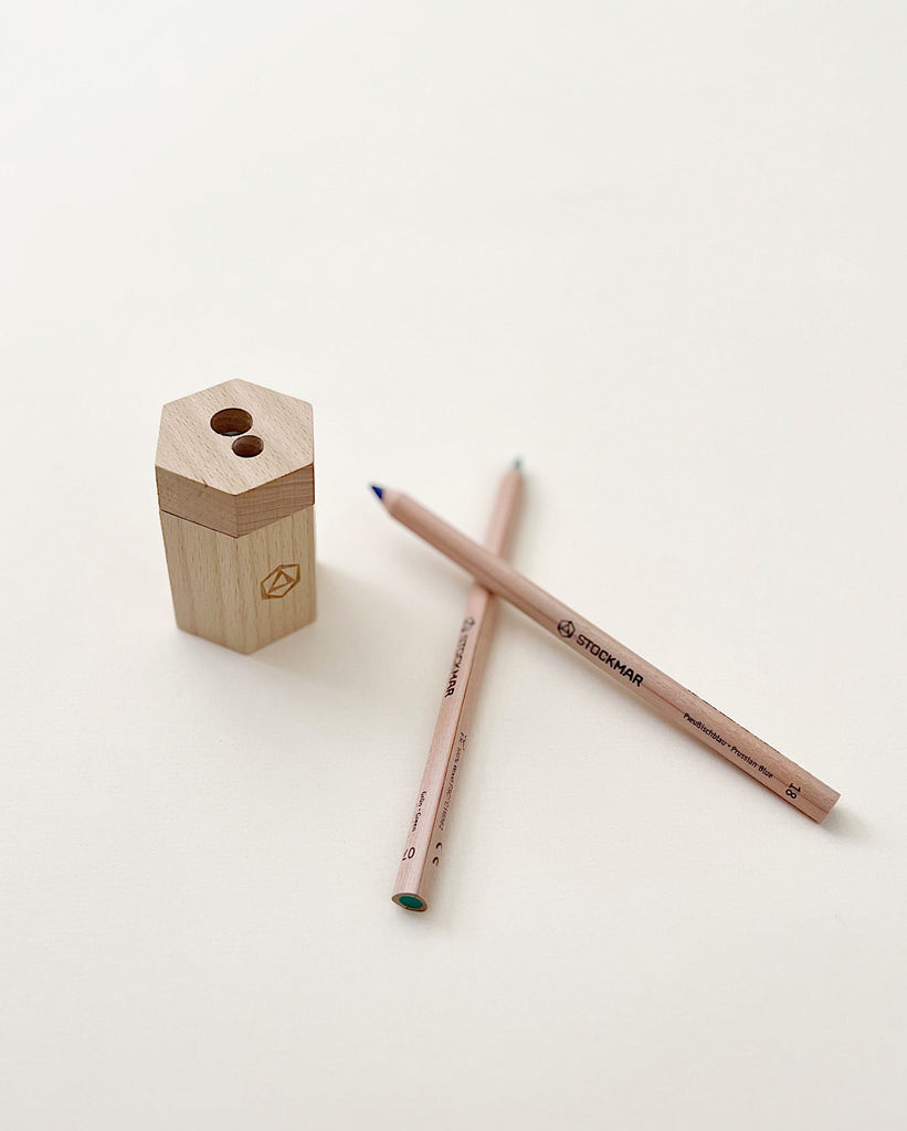 A Stockmar Dual Pencil Sharpener placed next to two Staedtler graphite pencils on a white background, one sharp and the other used with a blunt tip.