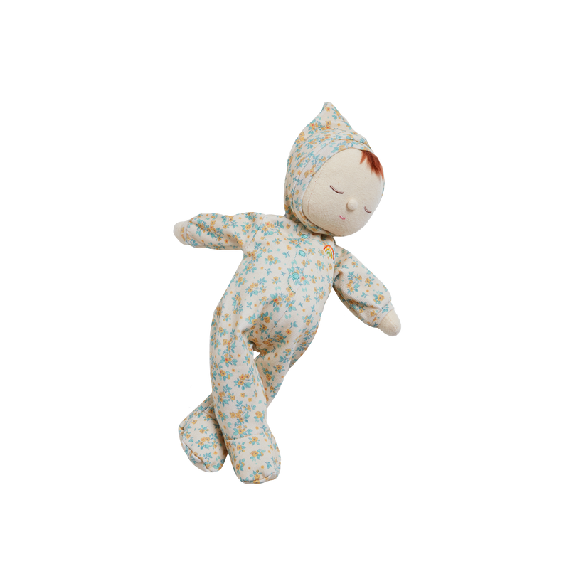 A Olli Ella Dozy Dinkum Doll - Daydream Edition with a floral pattern and a peaceful expression, wearing a matching hat, depicted against a transparent background. This limited edition item is crafted from 100% cotton.