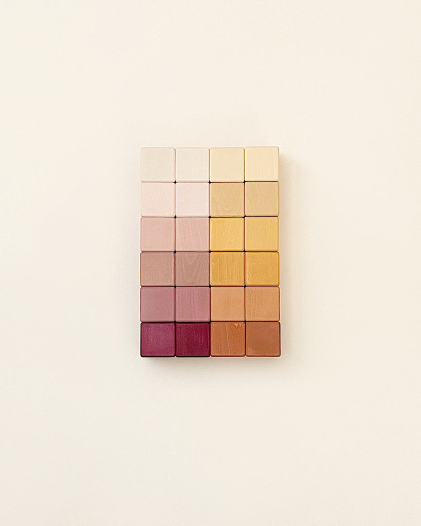 A grid of colorful square wooden blocks arranged in a gradient from white to deep red, coated with non-toxic paint, mounted on a light beige wall.