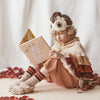 A young child dressed in a Meri Meri Owl Costume, complete with a crafted cape and wings, reads a book titled "Mice." They are seated among scattered autumn leaves on a soft, cream background.