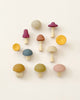 A collection of colorful, Raduga Grez Handmade Wooden Mushrooms arranged artistically on a light, solid background. The mushrooms vary in size and shade, featuring soft tones of yellow, blue, pink, and.