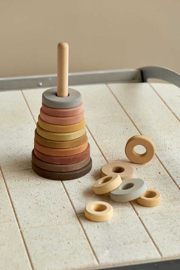 A Raduga Grez Handmade Large Pyramid Tower Stacker with various colored rings arranged on a pole, set on a speckled table. Some rings are on the table, while others are stacked on the pole.