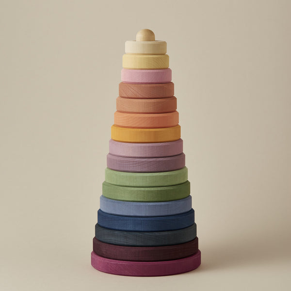 A Raduga Grez | Handmade Large Pyramid Tower Stacker in a gradient of colors ranging from purple at the base to peach at the top, against a neutral beige background. This toy is coated with non-toxic paint.