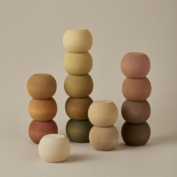 Three stacks of Raduga Grez Round Stackers in varying earth tones, neatly arranged by size on a neutral background. The left stack has six spheres, the middle seven, and the right six, with one sphere detached.