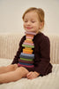 A young girl smiling with closed eyes, sitting on a white sofa, balancing a Raduga Grez | Handmade Large Pyramid Tower Stacker - Colorful on her neck. She wears a burgundy sweater dress.