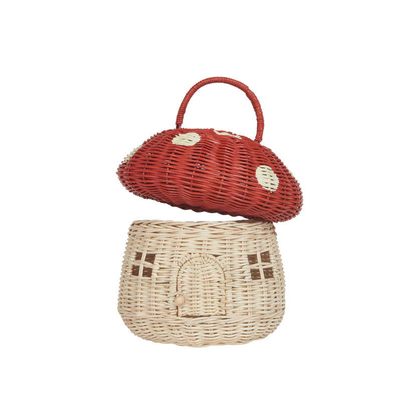 A decorative handmade Olli Ella Red Mushroom Basket, crafted from natural rattan, with a red cap and white spots on top, and a lighter colored base featuring a door and windows, resembling a small house.
