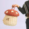 A person holding the Olli Ella | Red Mushroom Basket, featuring a small latch and window designs, against a light background.